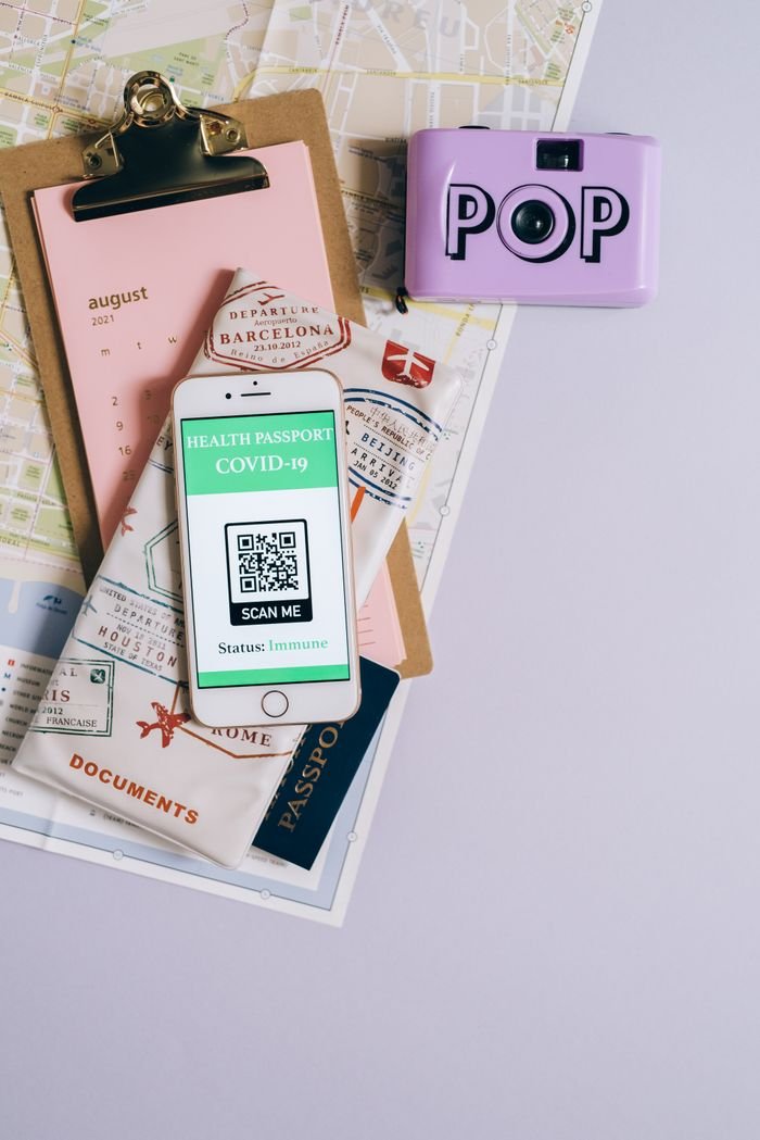 Flat lay of travel essentials with smartphone health passport, camera, map, and documents.